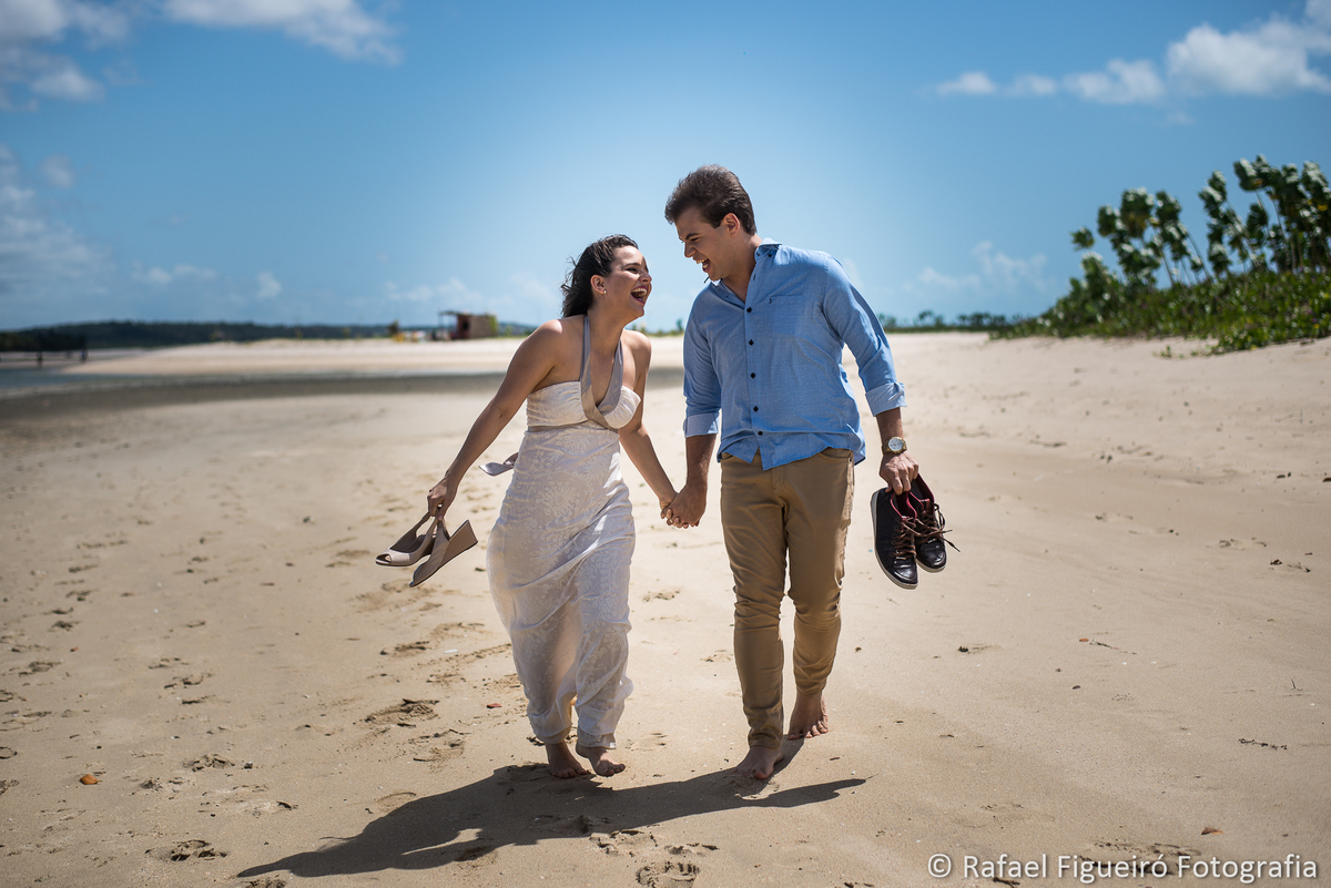 casal correndo se olhando sorrindo areia praia rio mangue sapatos nas mãos