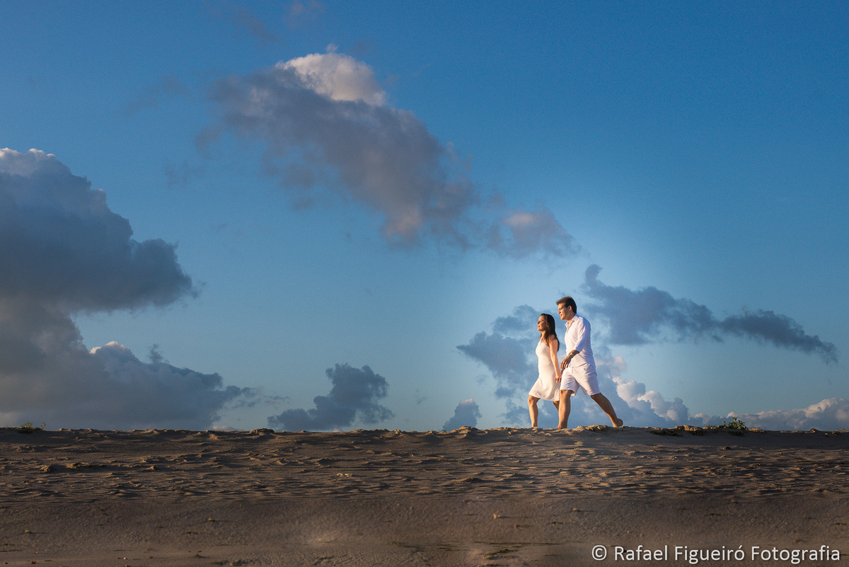 casal caminhando luz amarelada praia areia e céu azul com nuvens