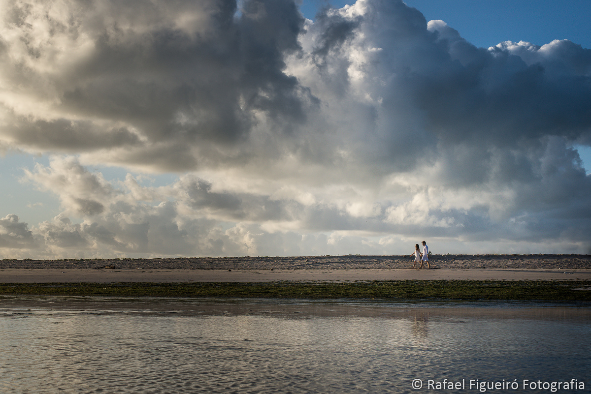 casal caminhando luz amarelada praia areia e céu azul com nuvens linda paisagem