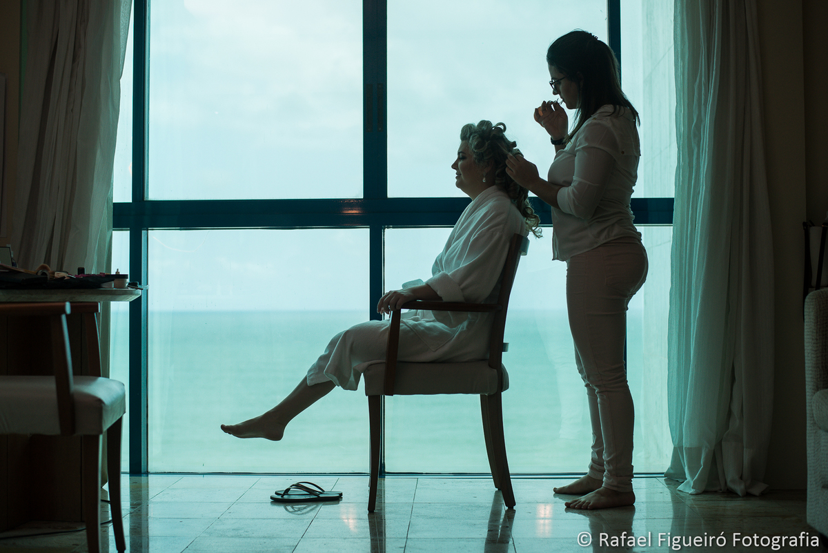 Maquiadora arrumando cabelo da noiva contra luz em frente janela