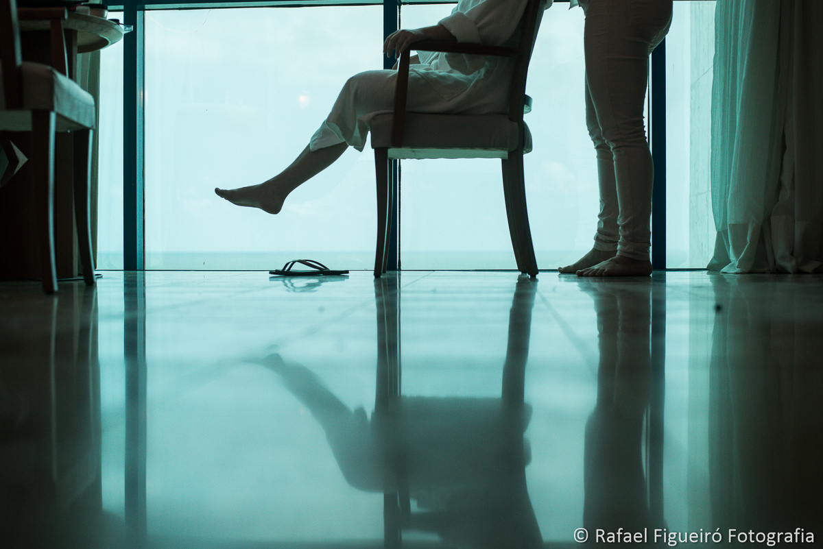 Noiva meio corpo sentada em cadeira contra luz janela maquiadora