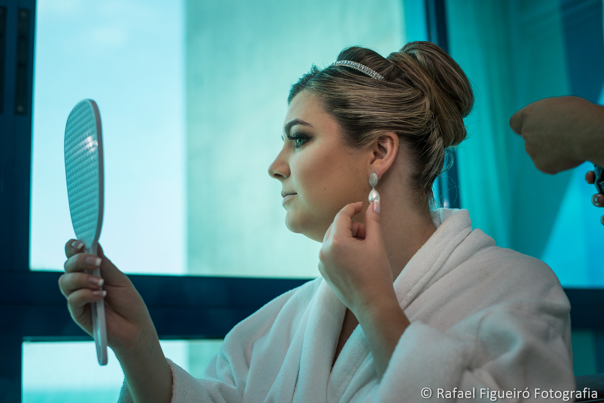 noiva olhando espelho de mão ajeitando brinco pérola