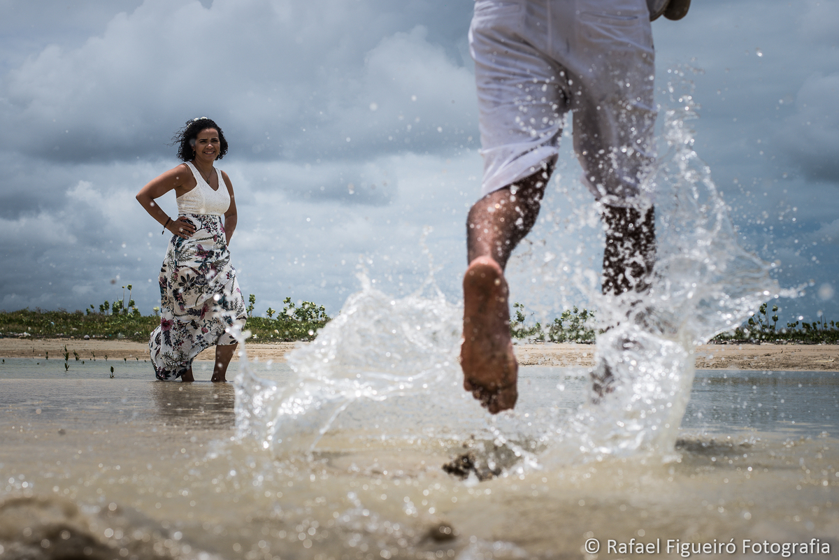 noiva em pé olhando noivo correndo sobre agua respingos maria farinha pontal praia céu nuvens rio timbó