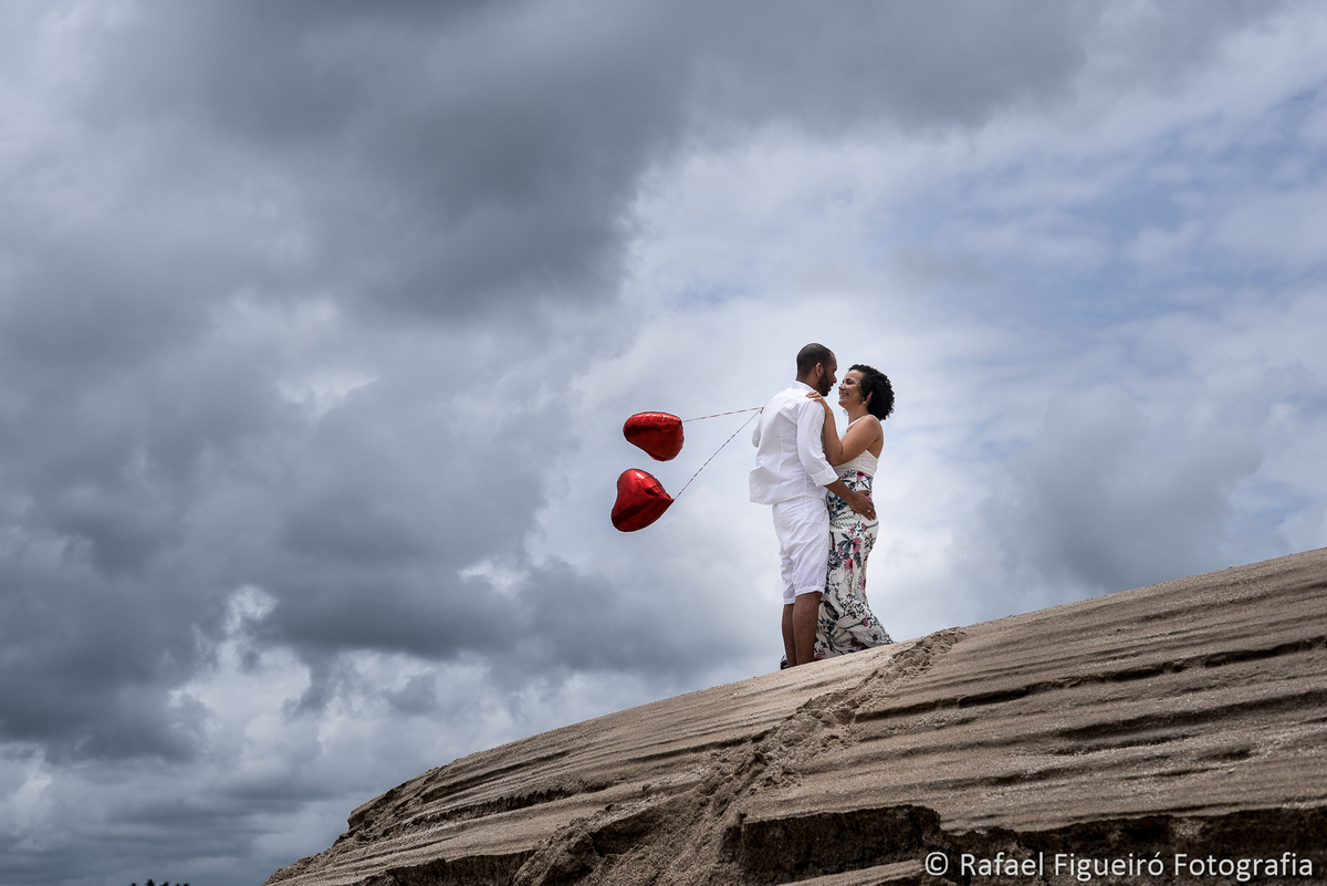 casal namorando sobre barranco de areia pontal maria farinha ceu nuvens balões coração vermelho rio timbó