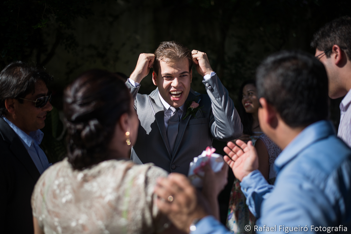 noivo alegre com maos na cabeça convidados ao redor