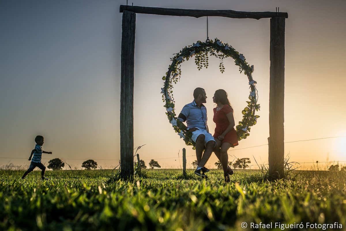 casal namorando sentado no balanço redondo flores menino correndo por do sol casa de campo