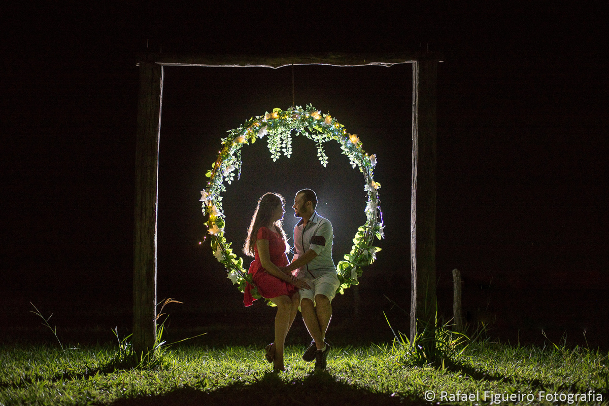 casal namorando sentado no balanço redondo flores casa de campo noite contra luz