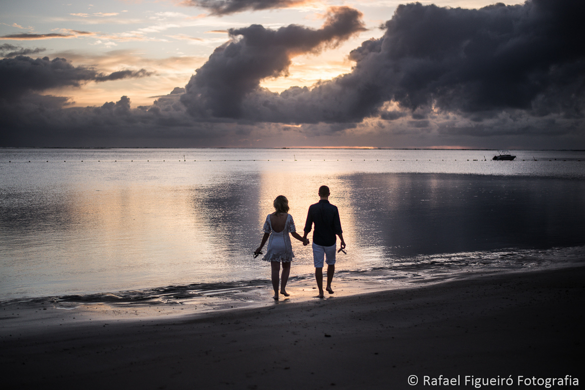 casal maos dadas praia por do sol contra luz carneiros