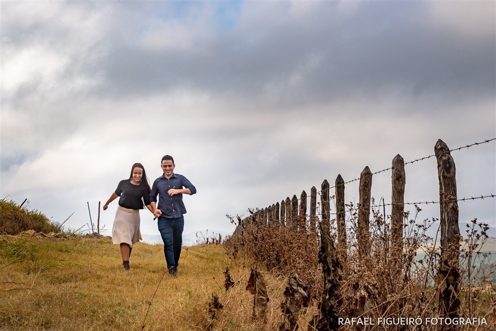 casal correndo estrada de grama cerca arame farpado maos dadas sorrindo felis amor