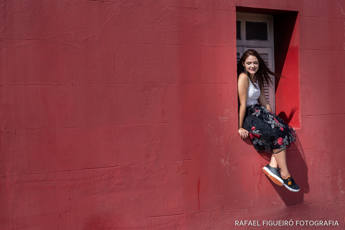 modelo debutante sentada janela madeira branca parede vermelha fundo recife antigo antiga estação pernas cruzadas cabelo voando