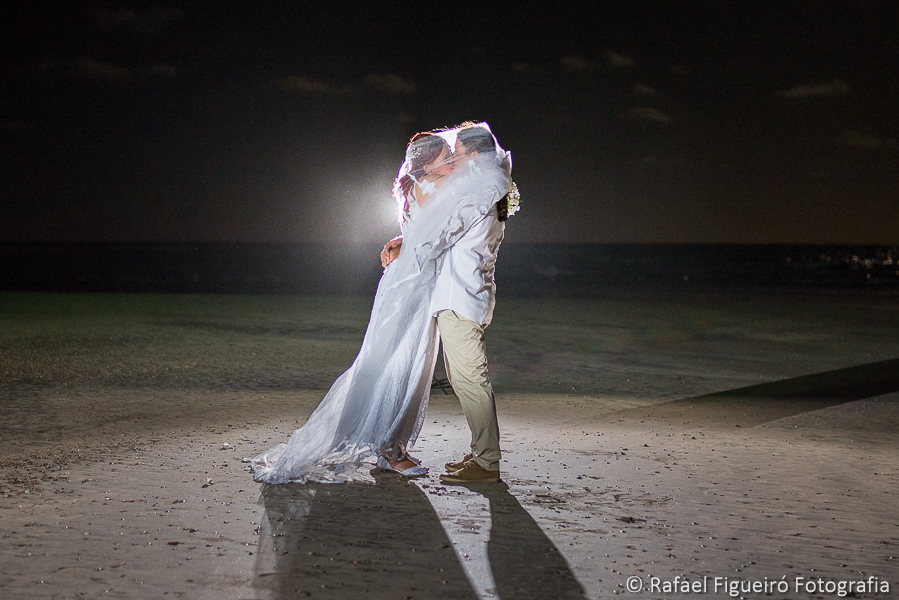 noivos se beijam cobertos pelo véu da noiva na praia do serrambí resort lua em destaque