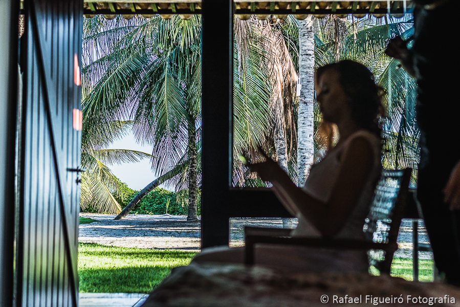 noiva em contra luz mexendo no seu Iphone com coqueiros ao fundo silhueta sombra serrambí resort fotografado por Rafael Figueiró fotógrafo de casamentos em Recife-PE pernambuco