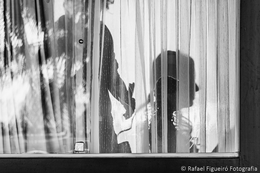 silhuetas do maquiador escovando os cabelos da noiva formados por um contra-luz nas cortinas da janela fotografado por Rafael Figueiró fotógrafo de casamentos em Recife-PE pernambuco