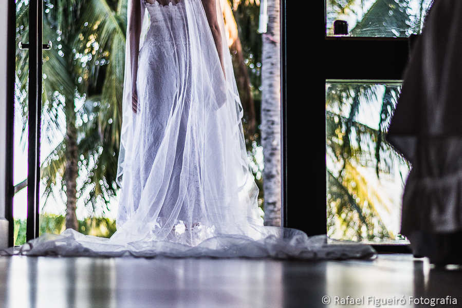detalhe da cauda e do véu do vestido da noiva saindo do quarto com coqueiros e praia na paisagem fora do quarto fotografado por Rafael Figueiró fotógrafo de casamentos em Recife-PE pernambuco