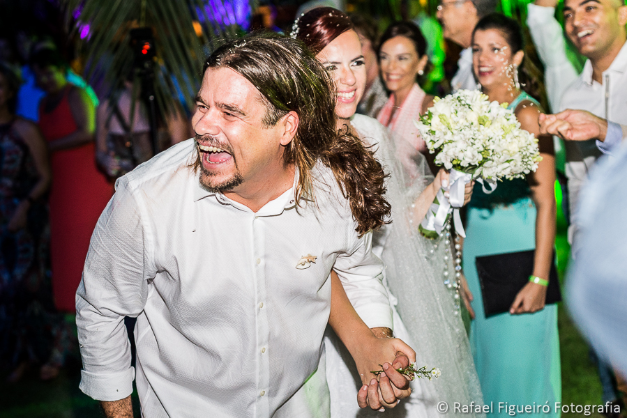 Noivo exaltado de alegria e descontração após chuva de arroz noiva ao fundo fotografado por Rafael Figueiró fotógrafo de casamentos em Recife-PE pernambuco