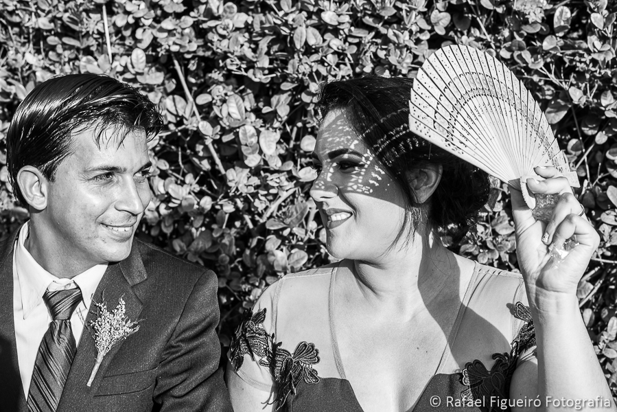 Madrinha e padrinho de casamento se olham madrinha com leque aparando o sol fotografado por Rafael Figueiró melhor fotógrafo de casamentos de Recife-PE