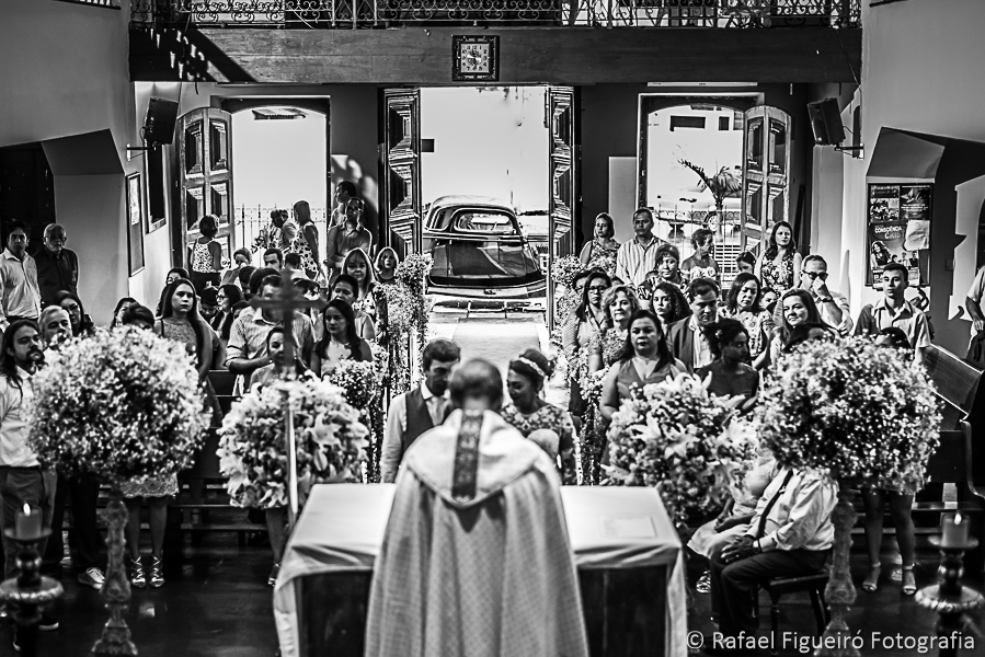 Noivos no altar casando padre de costas familiares assistindo carro antigo ao fundo na porta da igreja fotografado por Rafael Figueiró