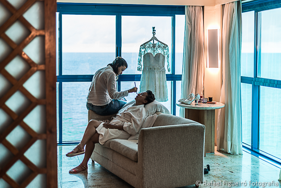 maquiadora produzindo a noiva no sofá do quarto com visual do mar ao fundo fotografado por Rafael Figueiró melhor fotógrafo de casamentos de Recife-PE