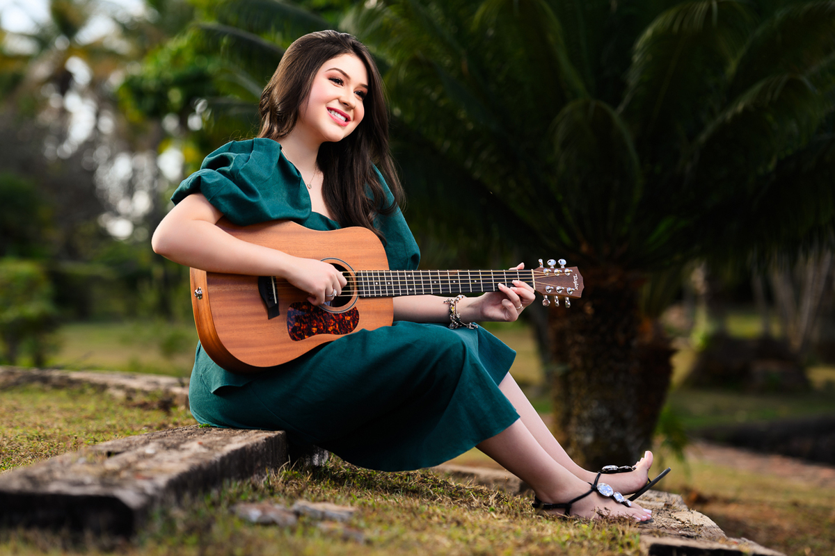 ensaio debutante violão sentada sob tronco de madeira em frente ao lago
