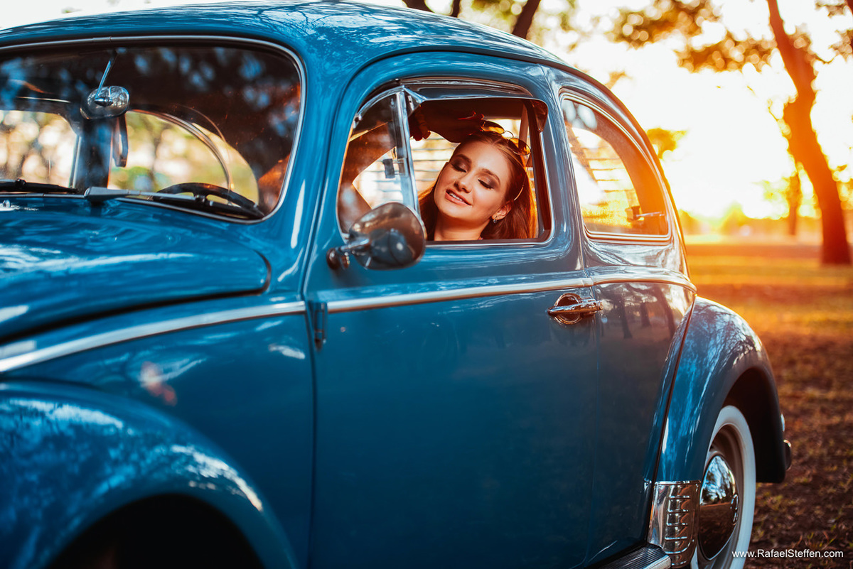 Foto do ensaio de quinze anos da Ester sentada dentro do fusca azul durante o pôr do sol em Brasília - DF.