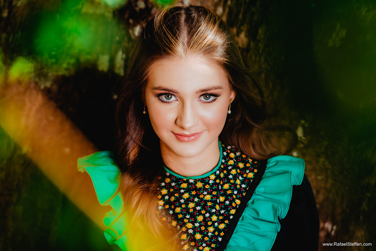 Ensaio de quinze anos da Ester sentada em frente a uma árvore com seu vestido de prenda.