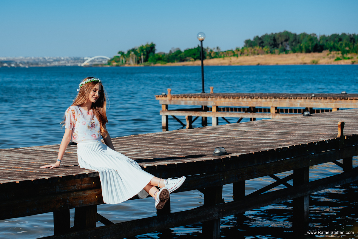 Foto do ensaio de quinze anos da Ester sentada no deck de madeira no lago sul em Brasília.