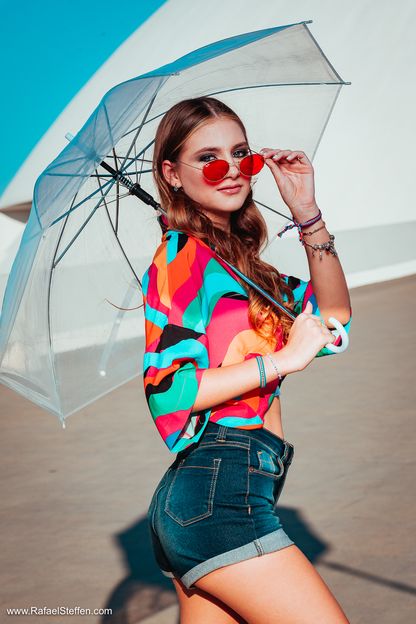 Foto de Debutante com sombrinha transparente segurando óculos de sol vermelho em frente ao Museu Nacional da República em Brasília DF.