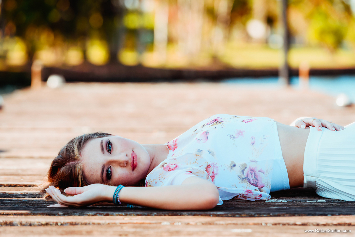 Foto do ensaio de quinze anos da Ester deitada sobre um deck de madeiro no lago sul em Brasília ohando para o lado.
