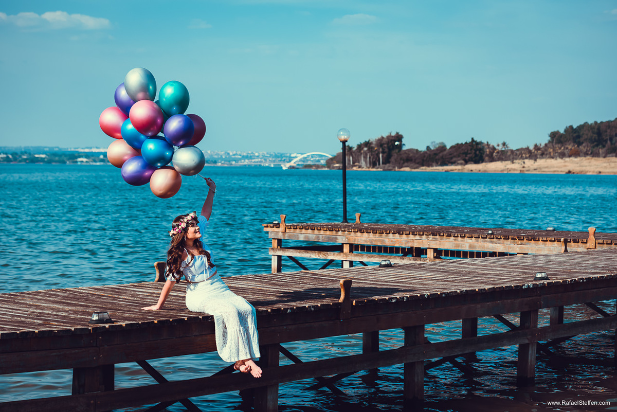 Foto de quinze anos segurando os balões sentada sobre deck de madeira no Lago Sul em Brasília - DF.