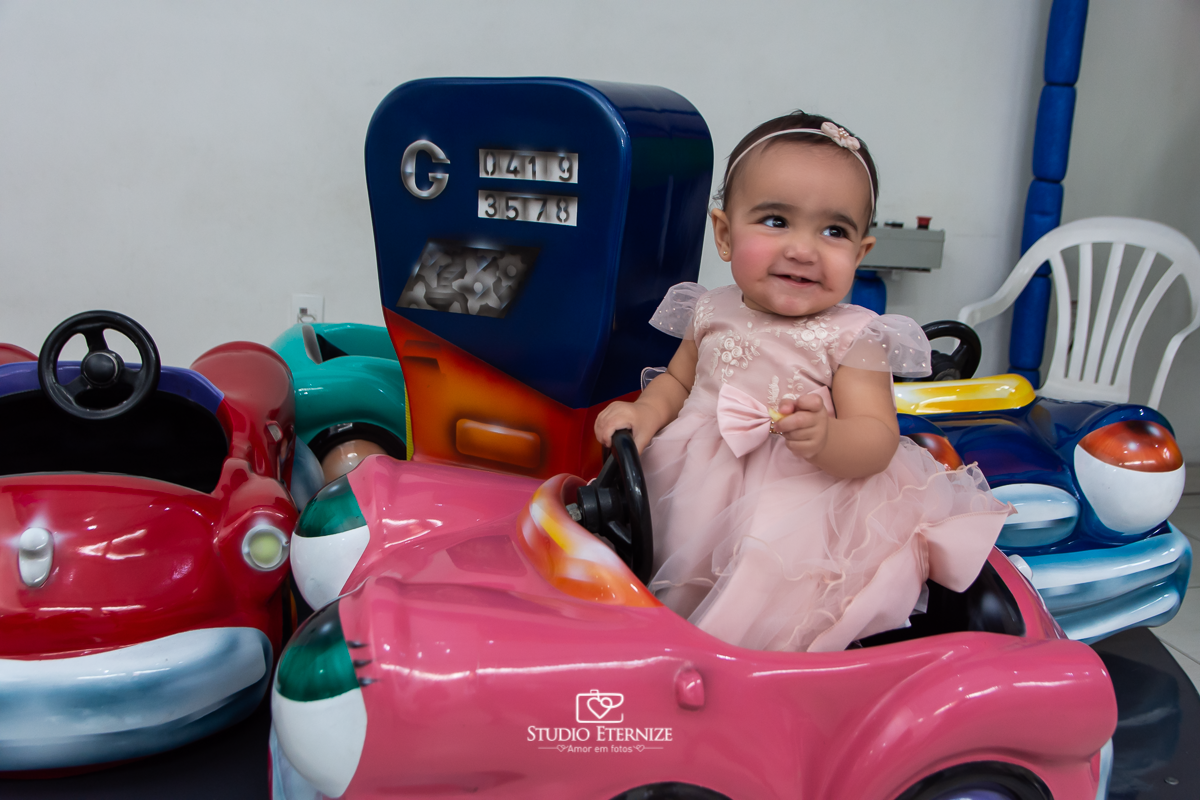 Fotografia da aniversariante brincando no carrossel de carros.