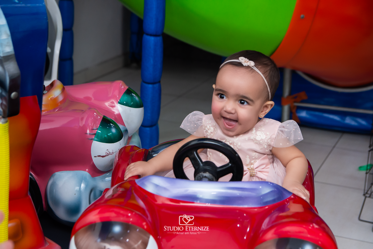 Fotografia da aniversariante brincando no carrossel de carros.