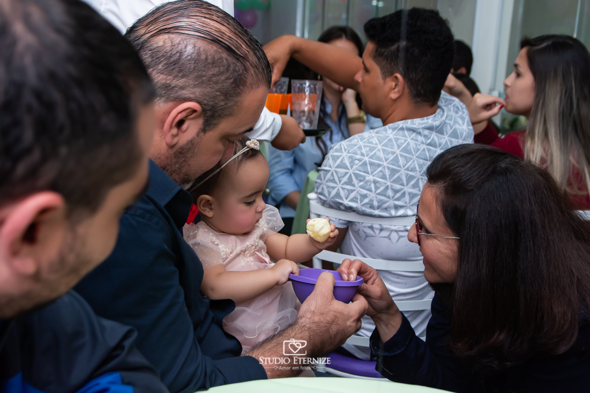 Fotografia da aniversariante fazendo um lanchinho no colo do papai.