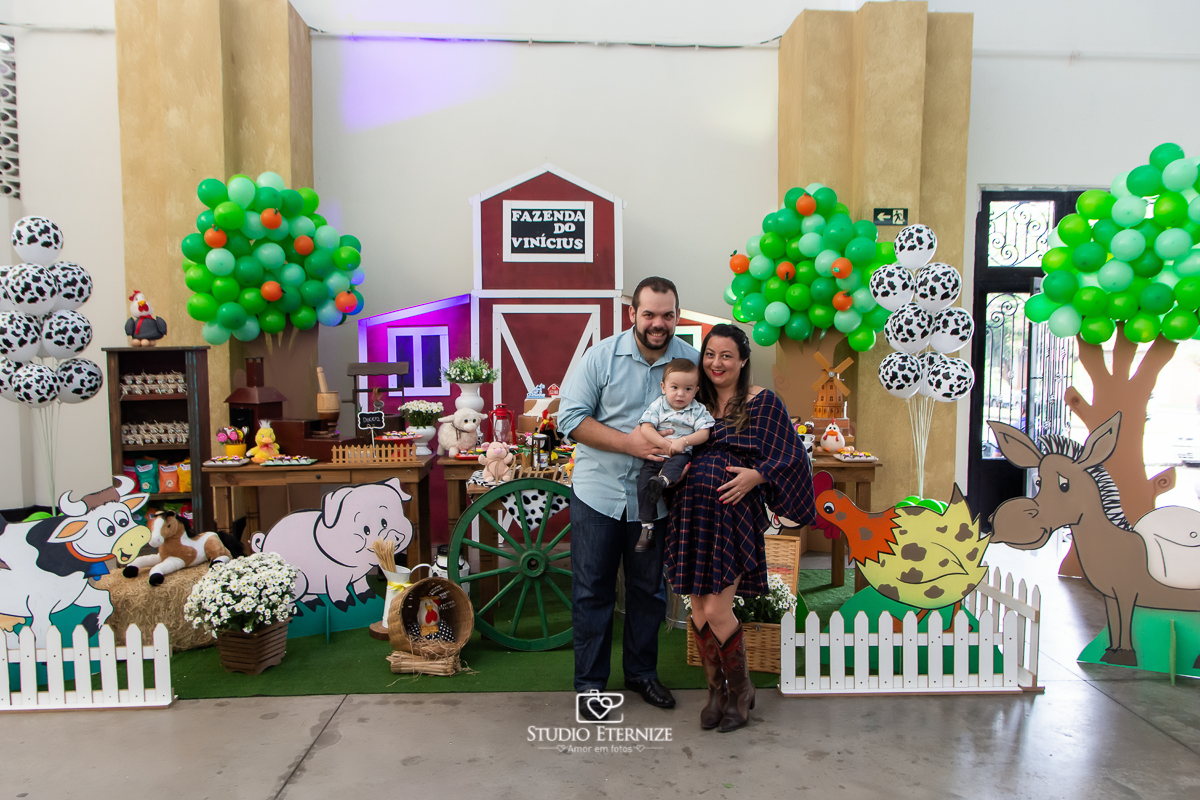 Fotografia de aniversario infantil no tema fazendinha realizado em Poços de Caldas. Pais e aniversariante posando para uma foto na frente da mesa do bolo.
