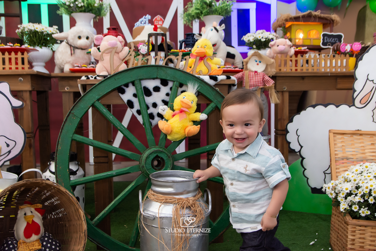 Fotografia de aniversario infantil no tema fazendinha realizado em Poços de Caldas. Aniversariante brincando com a leiteira na frente da mesa do bolo.