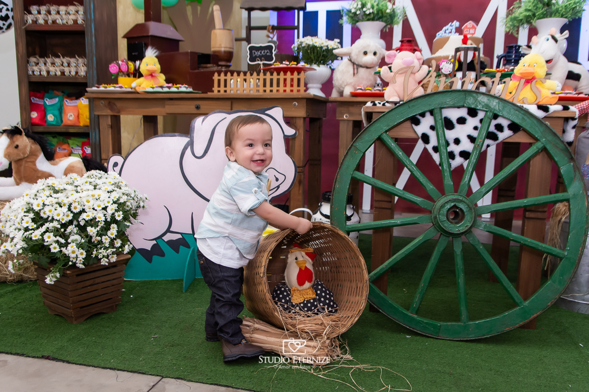 Fotografia de aniversario infantil no tema fazendinha realizado em Poços de Caldas. Aniversariante brincando com um balaio na frente da mesa do bolo.