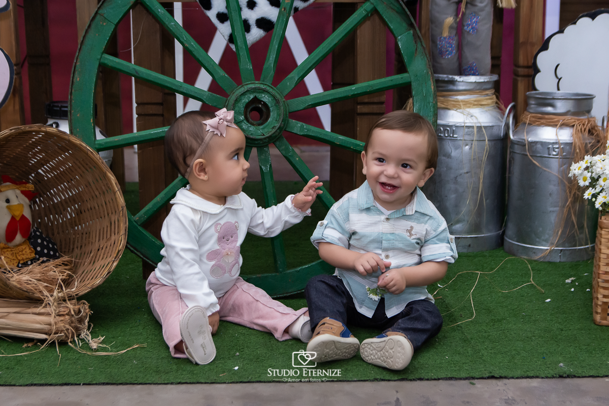 Fotografia de aniversario infantil no tema fazendinha realizado em Poços de 
 Caldas. Aniversariante posando para uma foto na frente da mesa do bolo com uma amiguinha. 