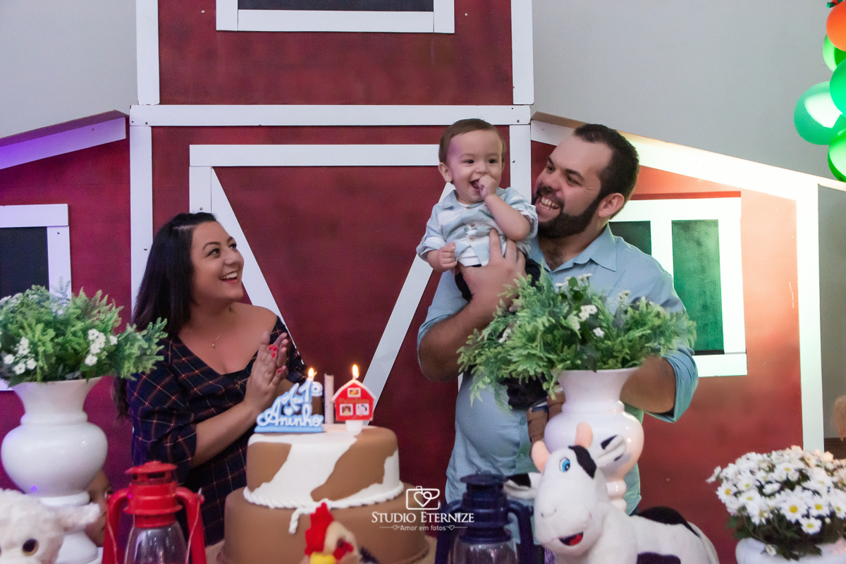 Fotografia de aniversario infantil no tema fazendinha realizado em Poços de Caldas. Pais e aniversariante na mesa do bolo cantando parabéns.
