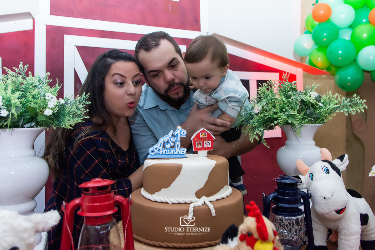 Fotografia de aniversario infantil no tema fazendinha realizado em Poços de Caldas. Pais e aniversariante na mesa do bolo soprando a velhinha.