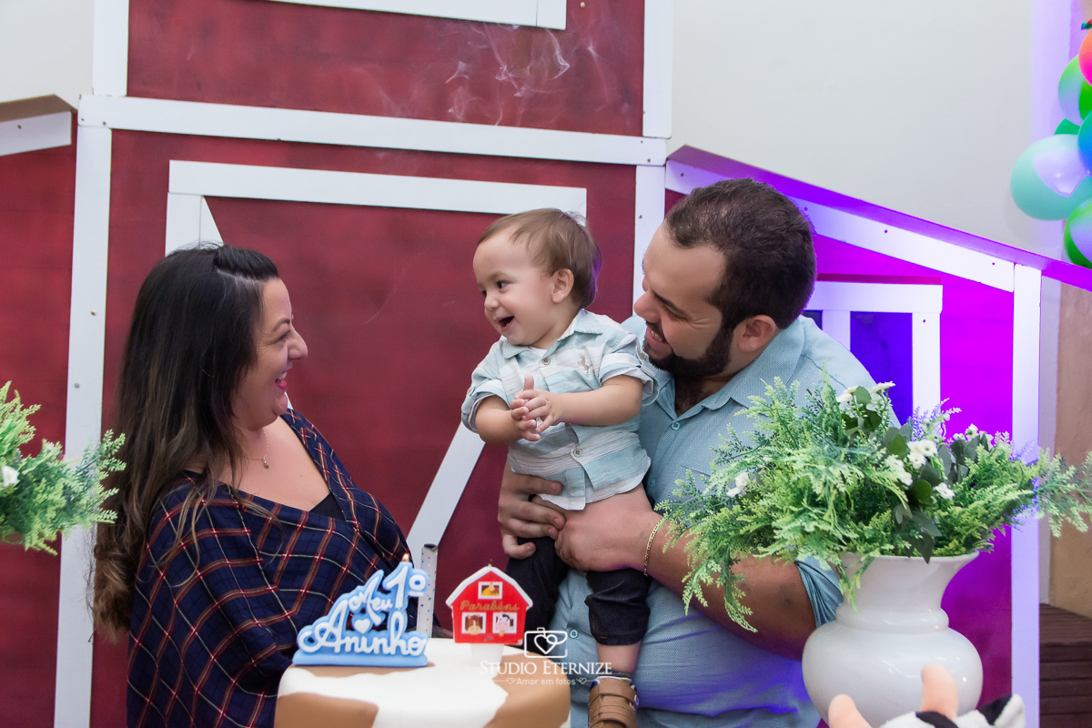 Fotografia de aniversario infantil no tema fazendinha realizado em Poços de Caldas. Pais fazendo e aniversariante se divertem na mesa do bolo.