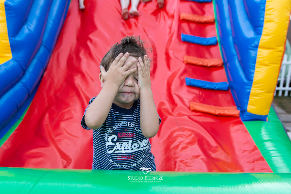 Fotografia de aniversário infantil realizado pelo Studio Eternize em Poços de Caldas. Tema da festa cientista. Irmão do aniversariante brincando com as mãos de esconder.