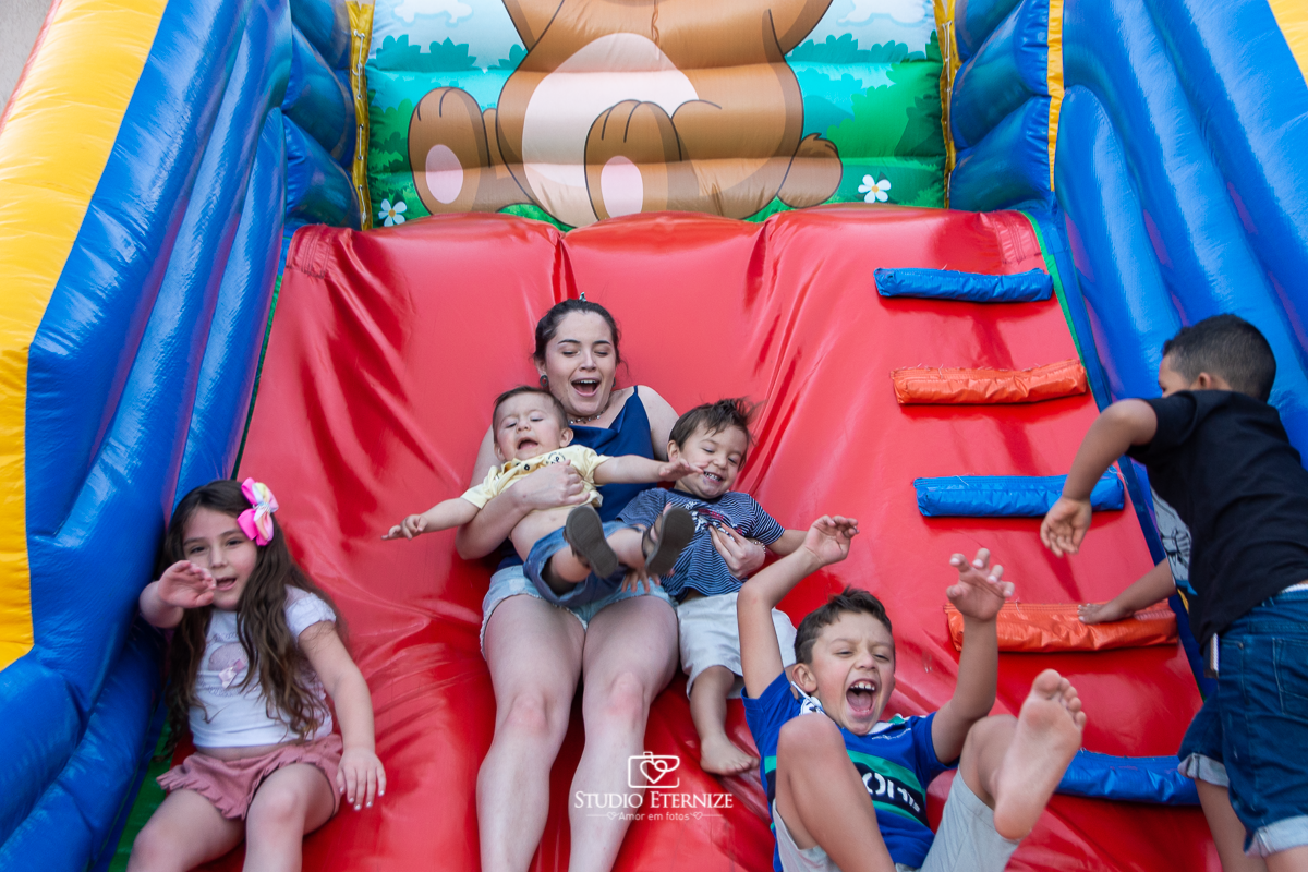 Fotografia de aniversário infantil realizado pelo Studio Eternize em Poços de Caldas. Tema da festa cientista. Aniversariante e seu irmão no colo de sua prima e seus primos ao lado escorregando.