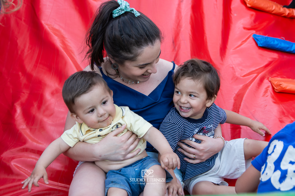 Fotografia de aniversário infantil realizado pelo Studio Eternize em Poços de Caldas. Tema da festa cientista. Close do aniversariante e seu irmão no colo de sua prima e seus primos ao lado escorregando.