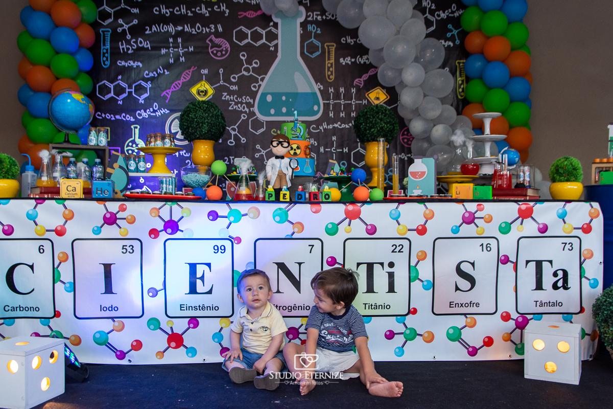 Fotografia de aniversário infantil realizado pelo Studio Eternize em Poços de Caldas. Tema da festa cientista. Aniversariante e seu irmão posando para a foto em frente a mesa do bolo.