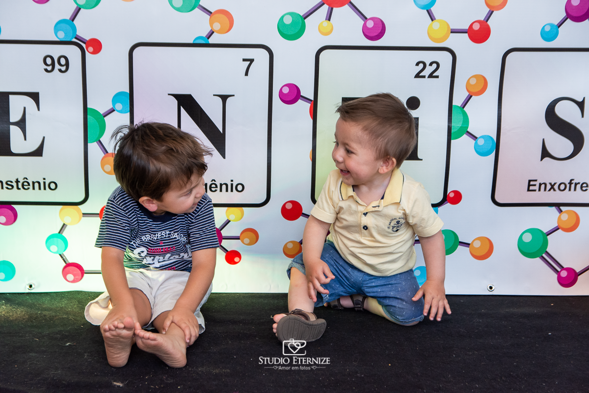 Fotografia de aniversário infantil realizado pelo Studio Eternize em Poços de Caldas. Tema da festa cientista. Aniversariante olhando para seu irmão e posando para a foto em frente a mesa do bolo.