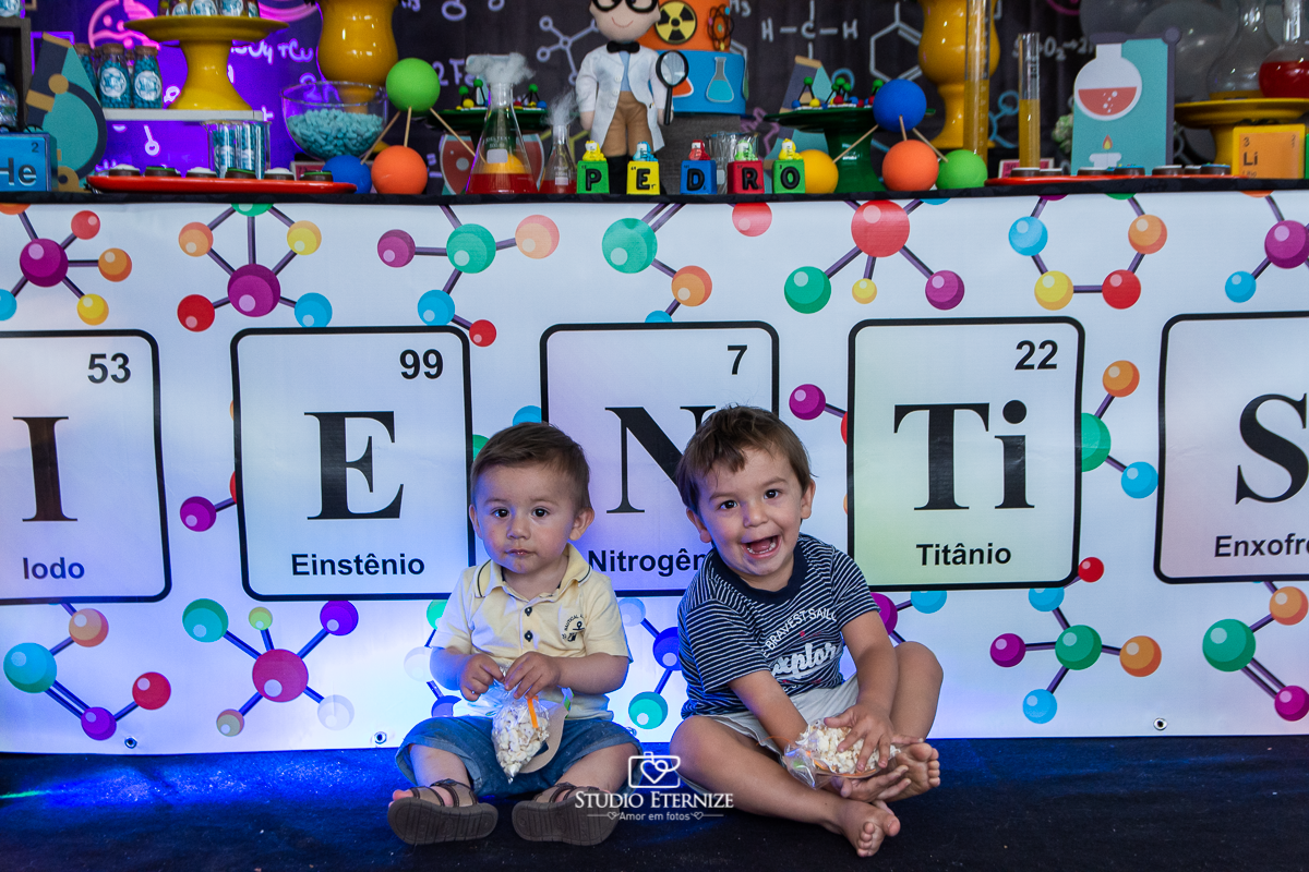 Fotografia de aniversário infantil realizado pelo Studio Eternize em Poços de Caldas. Tema da festa cientista. Close do aniversariante e seu irmão posando para a foto em frente a mesa do bolo.