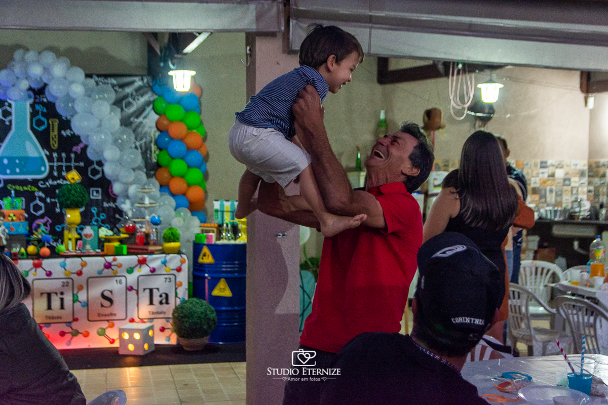 Fotografia de aniversário infantil realizado pelo Studio Eternize em Poços de Caldas. Tema da festa cientista. Irmão do aniversariante brincando com seu avô.