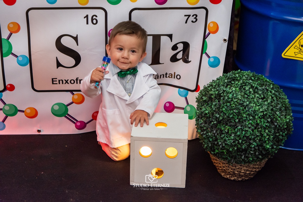 Fotografia de aniversário infantil realizado pelo Studio Eternize em Poços de Caldas. Tema da festa cientista. Aniversariante brincando com a decoração e olhando para a foto.