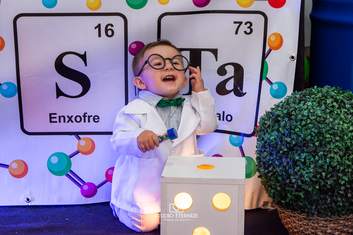 Fotografia de aniversário infantil realizado pelo Studio Eternize em Poços de Caldas. Tema da festa cientista. Aniversariante de óculos e brincando com a decoração.