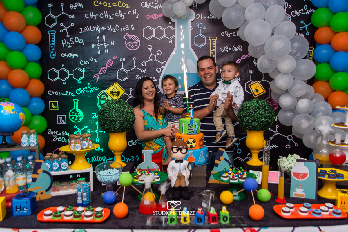 Fotografia de aniversário infantil realizado pelo Studio Eternize em Poços de Caldas. Tema da festa cientista. Aniversariante, seu irmão e seus pais cantando parabéns.