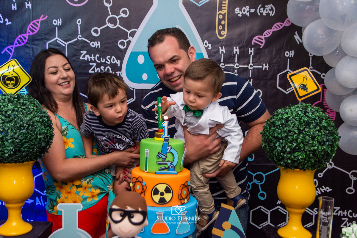Fotografia de aniversário infantil realizado pelo Studio Eternize em Poços de Caldas. Tema da festa cientista. Aniversariante, seus pais e seu irmão soprando a vela.
